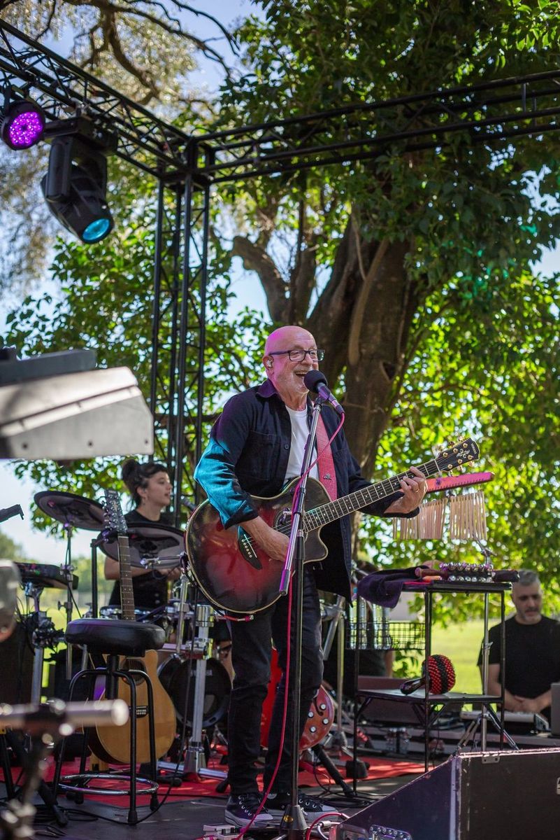 Juan Carlos Baglietto cantando con la guitarra y la banda en vivo detr&aacute;s en el escenario