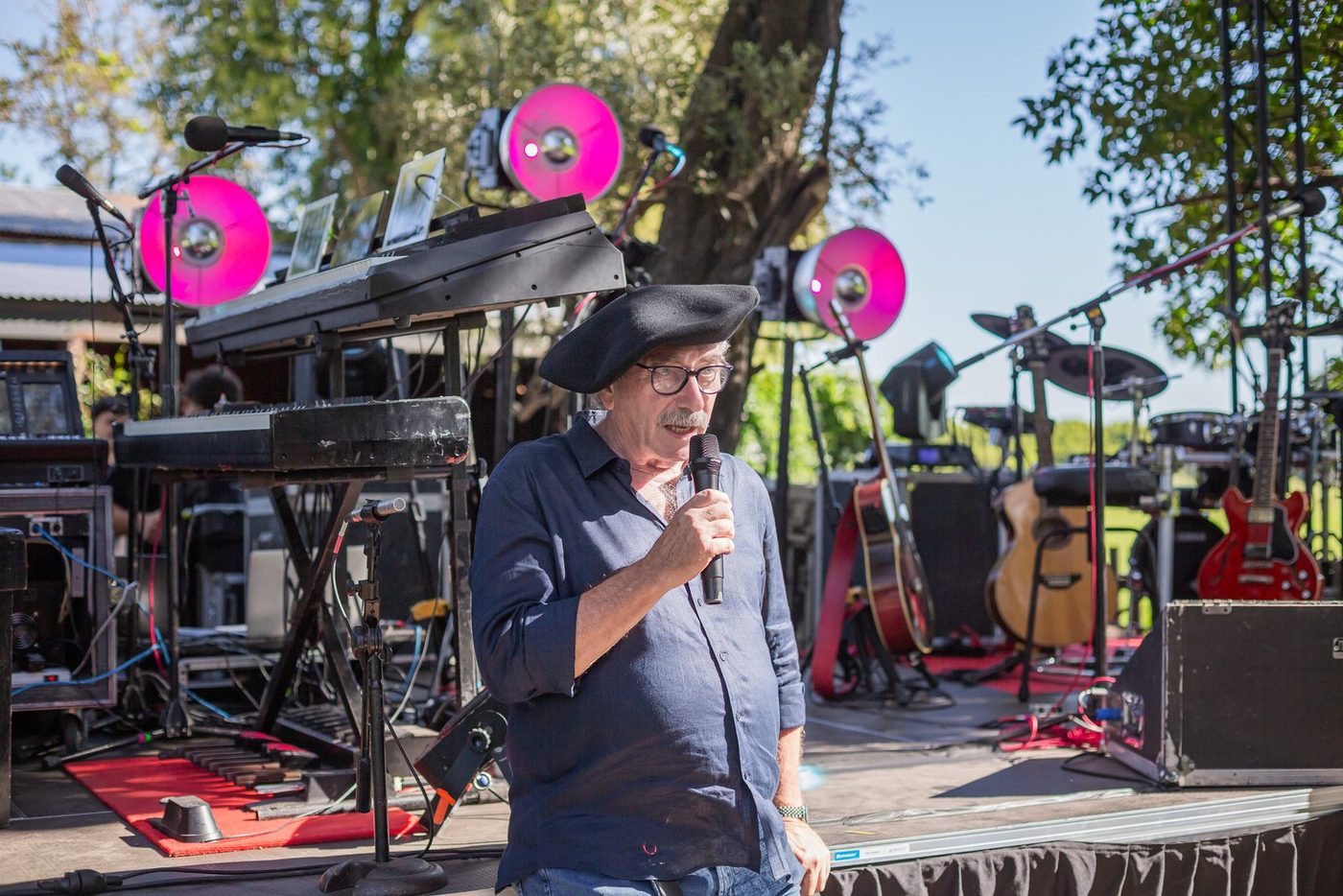 Un invitado con boina hablando por micr&oacute;fono frente al escenario montado con las luces fucsias