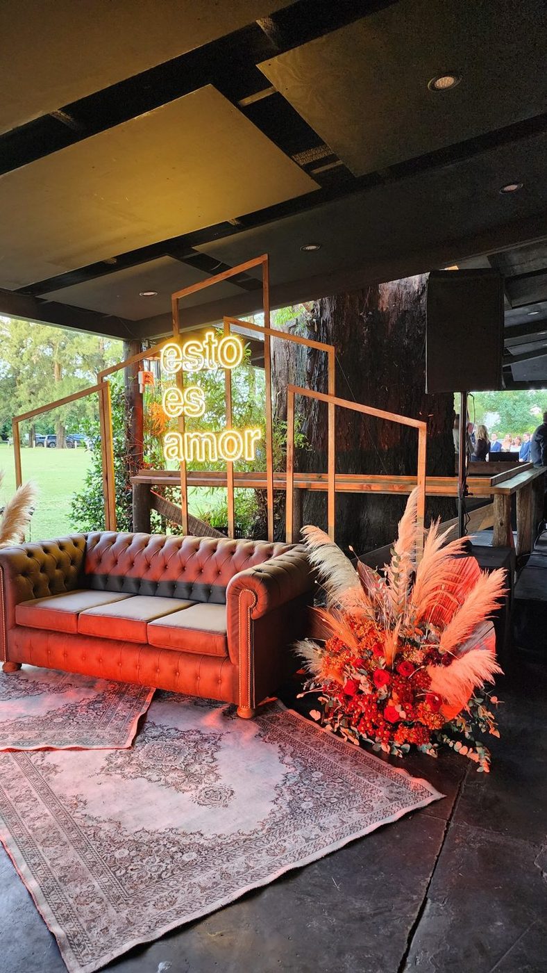 Sector lounge de una boda con cartel de neón, sillón y ambientación floral