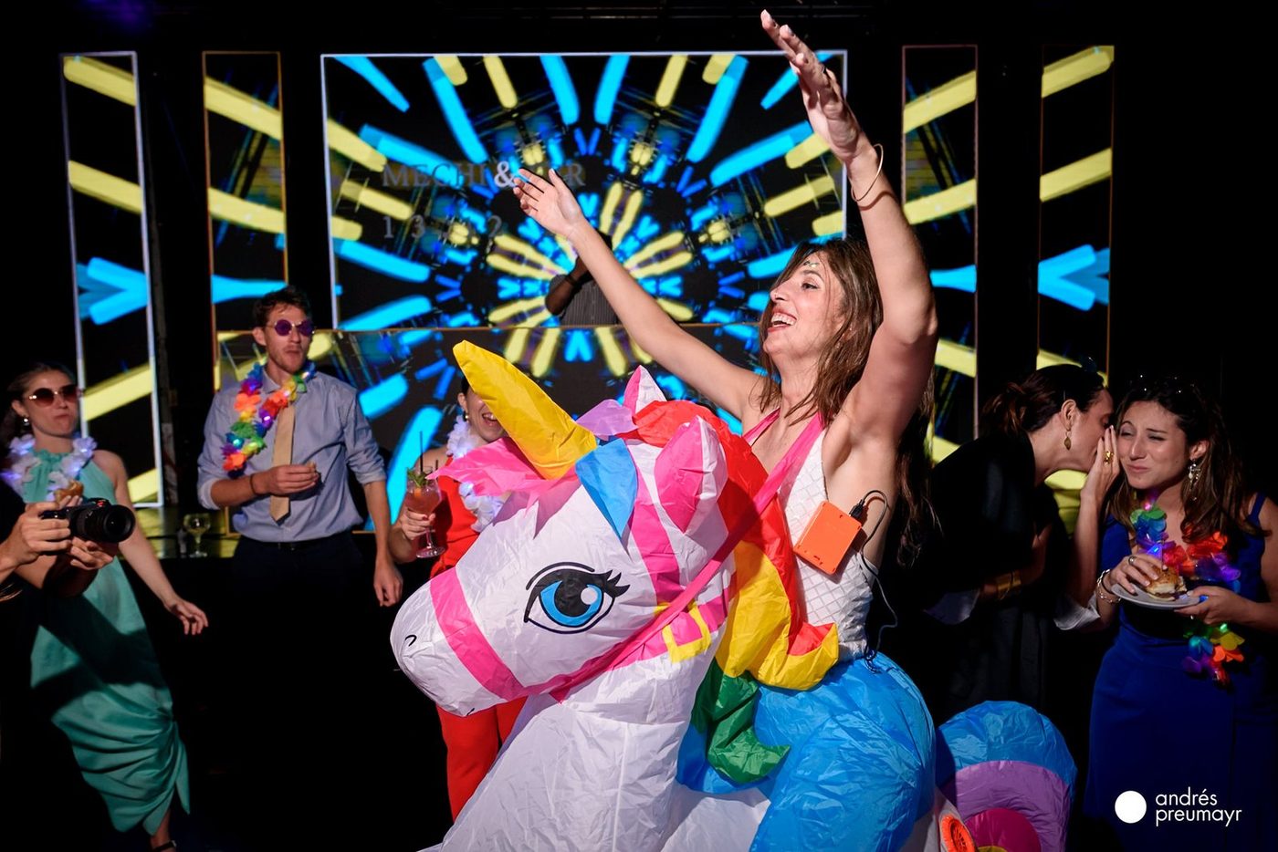 Invitados bailando con disfraces inflables en la pista, con pantalla LED de fondo