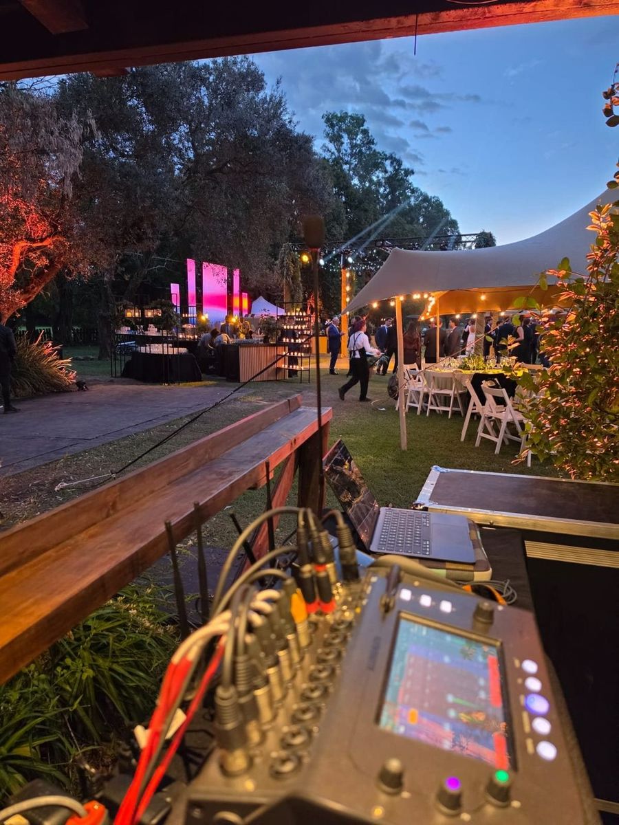 Consola de sonido en el puesto de operaci&oacute;n con el escenario iluminado de fondo al anochecer