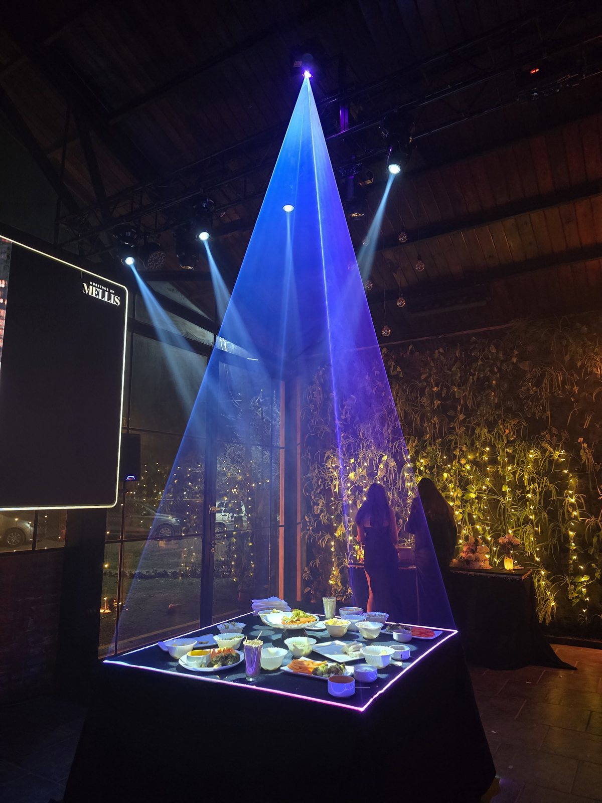 Mesa de bocaditos con el borde iluminado por l&aacute;ser y haces de luz en la recepci&oacute;n